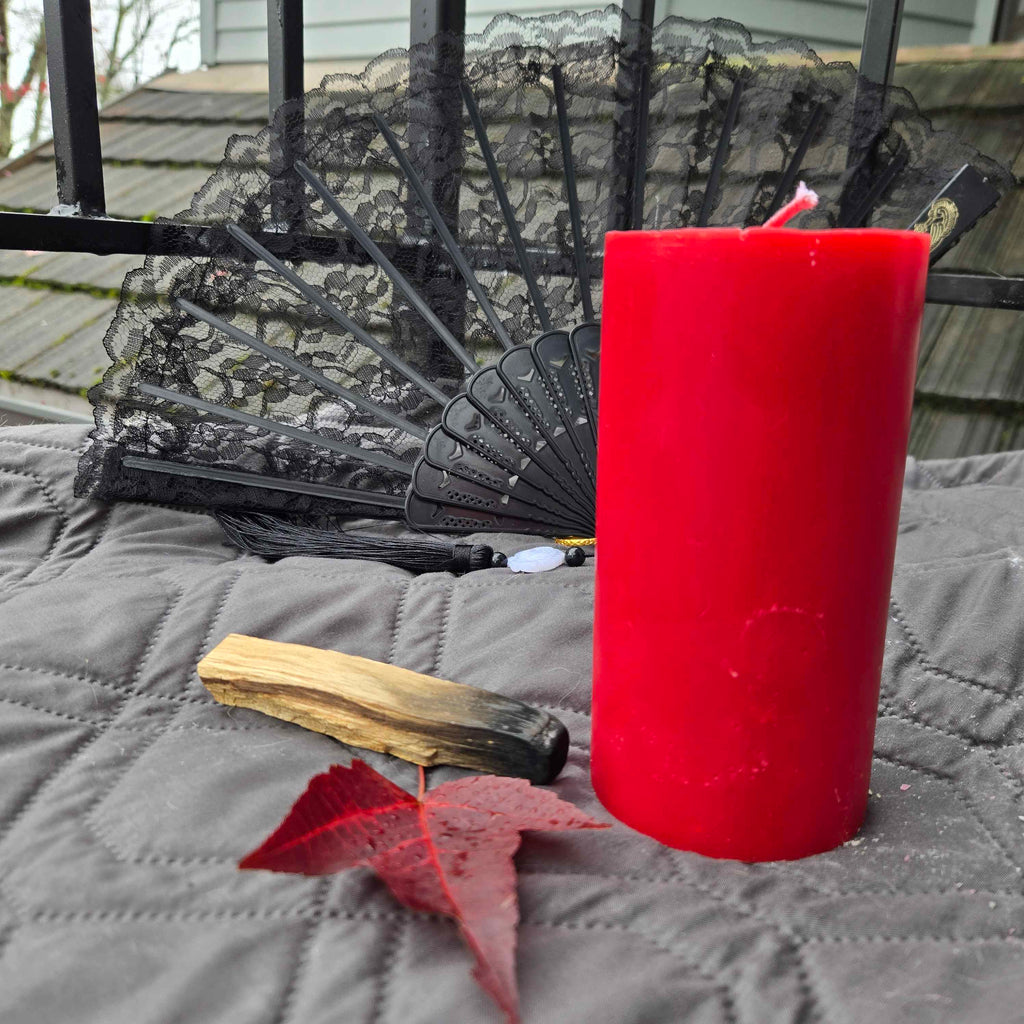 Red candle with a black lace fan, wooden stick, and red leaf on a gray surface.