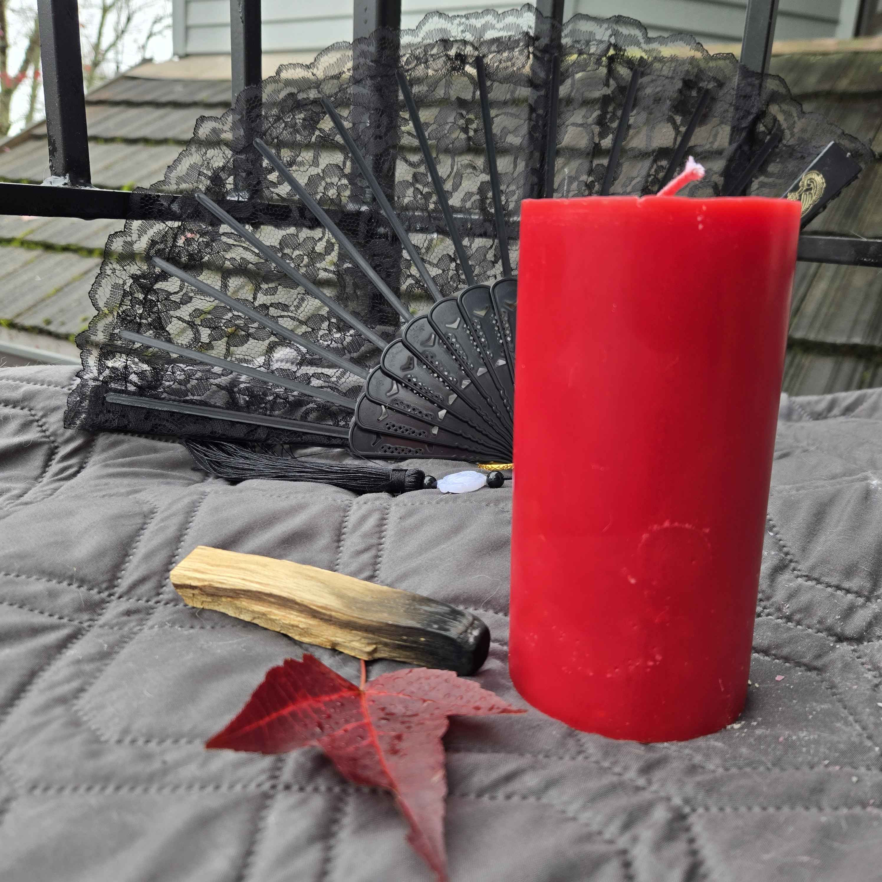 Red candle with a black lace fan, wooden stick, and red leaf on a gray surface.